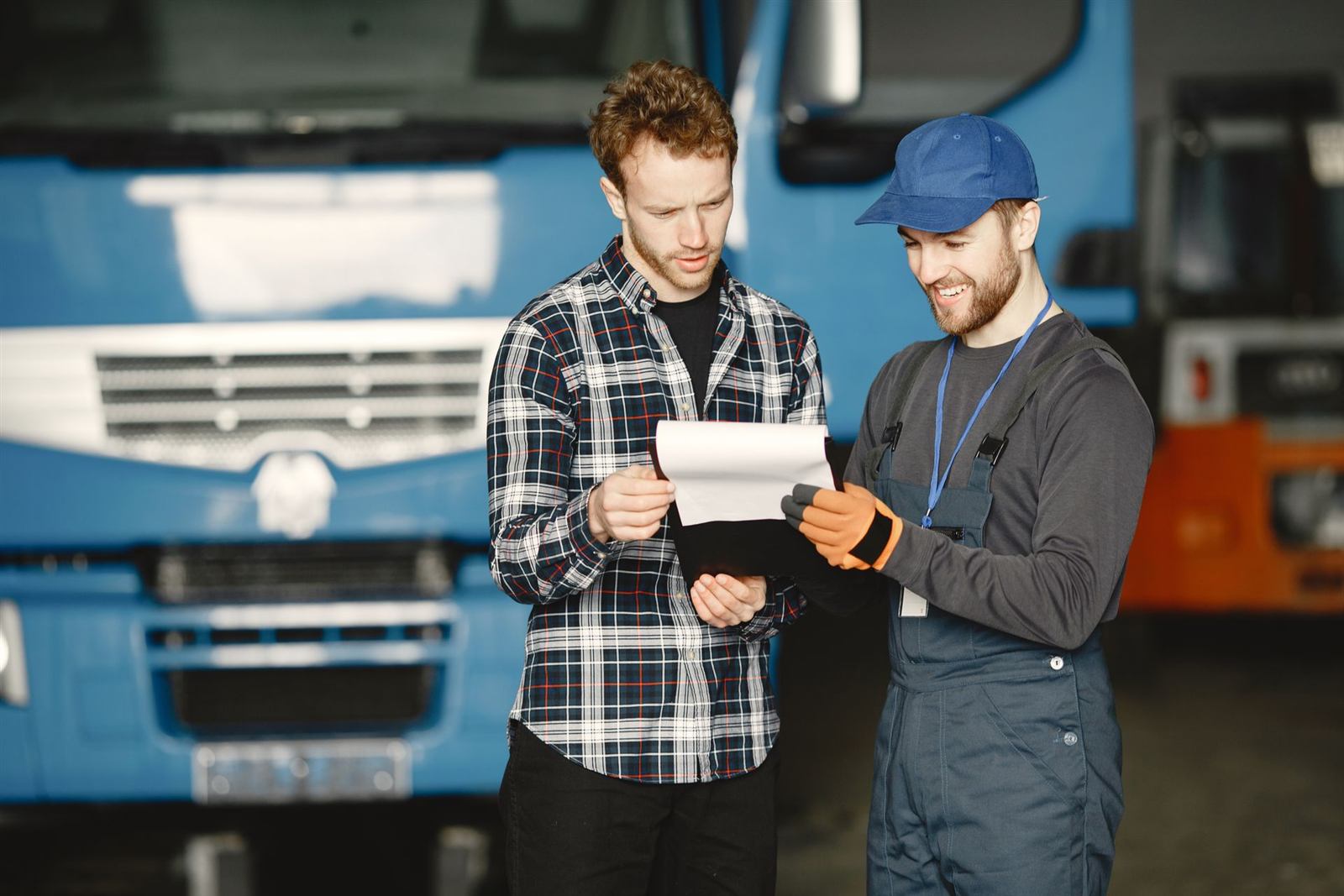 Transport manager and mechanic checking maintenance paperwork in a truck garage